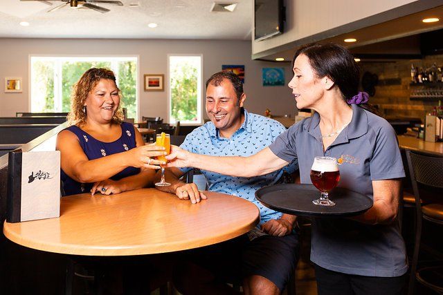 A woman is serving a drink to a man and woman at a restaurant.