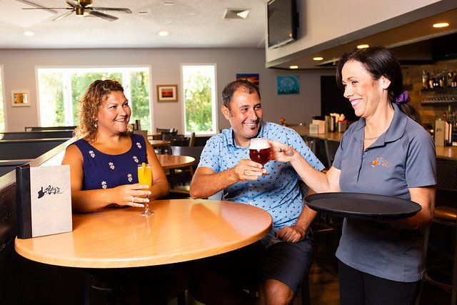 A woman is serving a drink to a man and a woman at a restaurant.