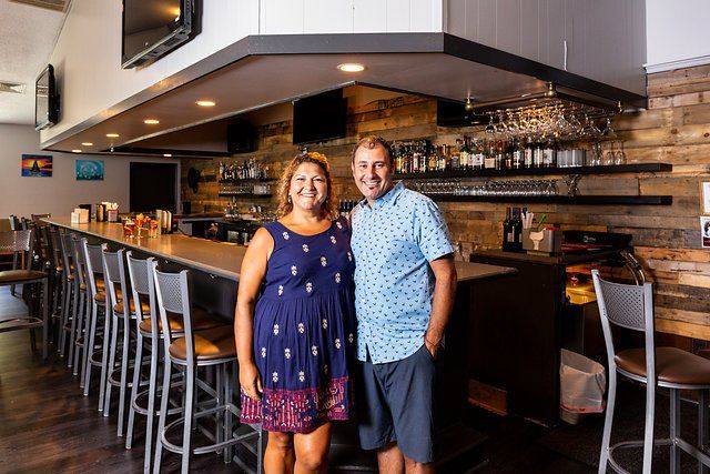 A man and a woman are standing in front of a bar in a restaurant.