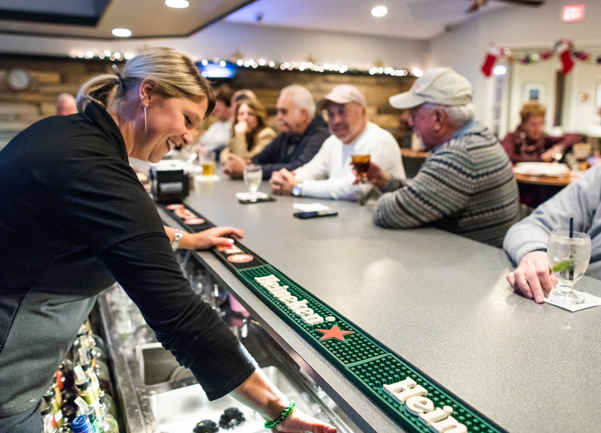 A woman is serving a heineken beer at a bar