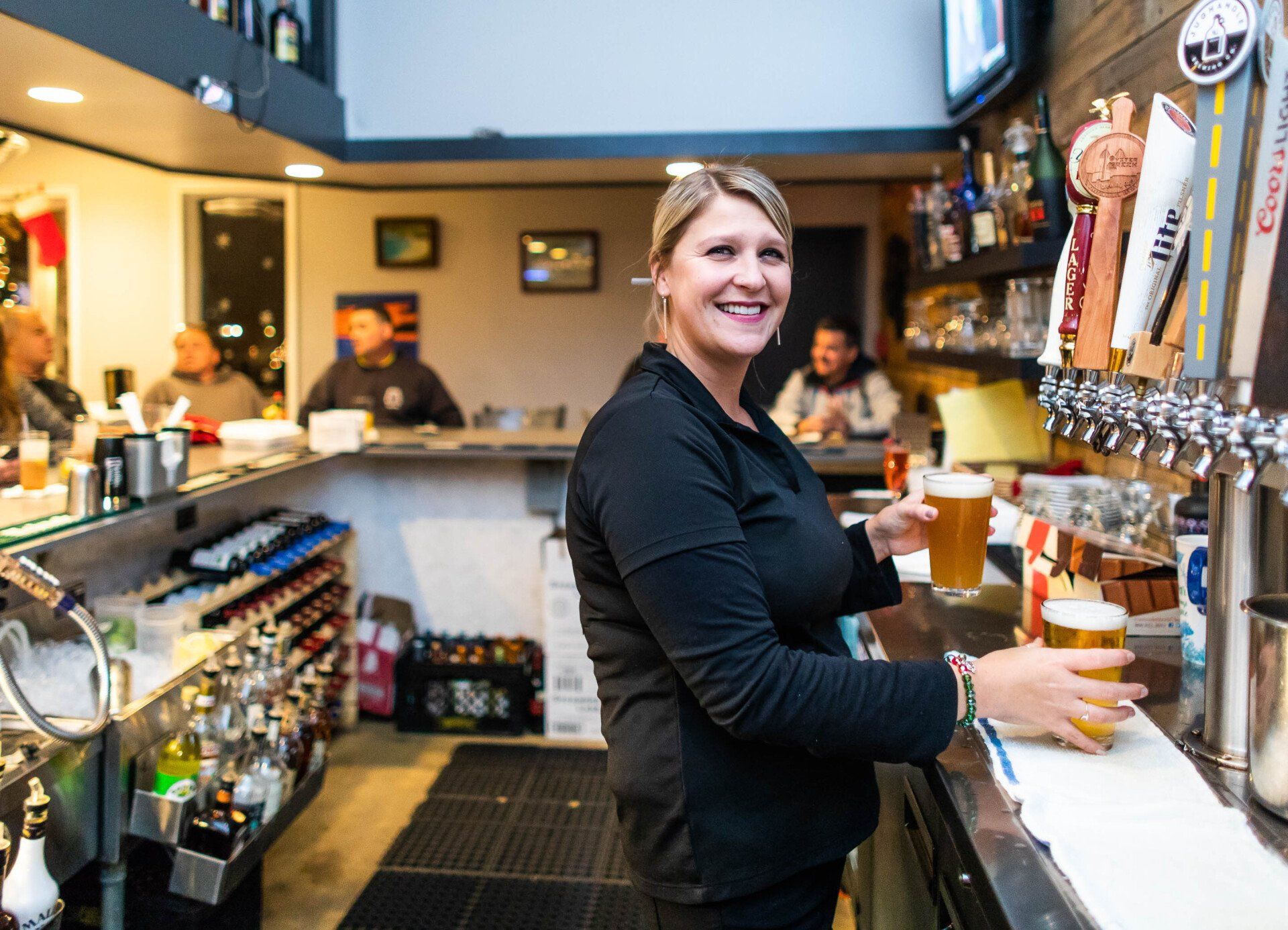 A woman is standing at a bar holding a glass of beer.