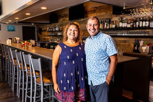 A man and a woman are standing in front of a bar in a restaurant.