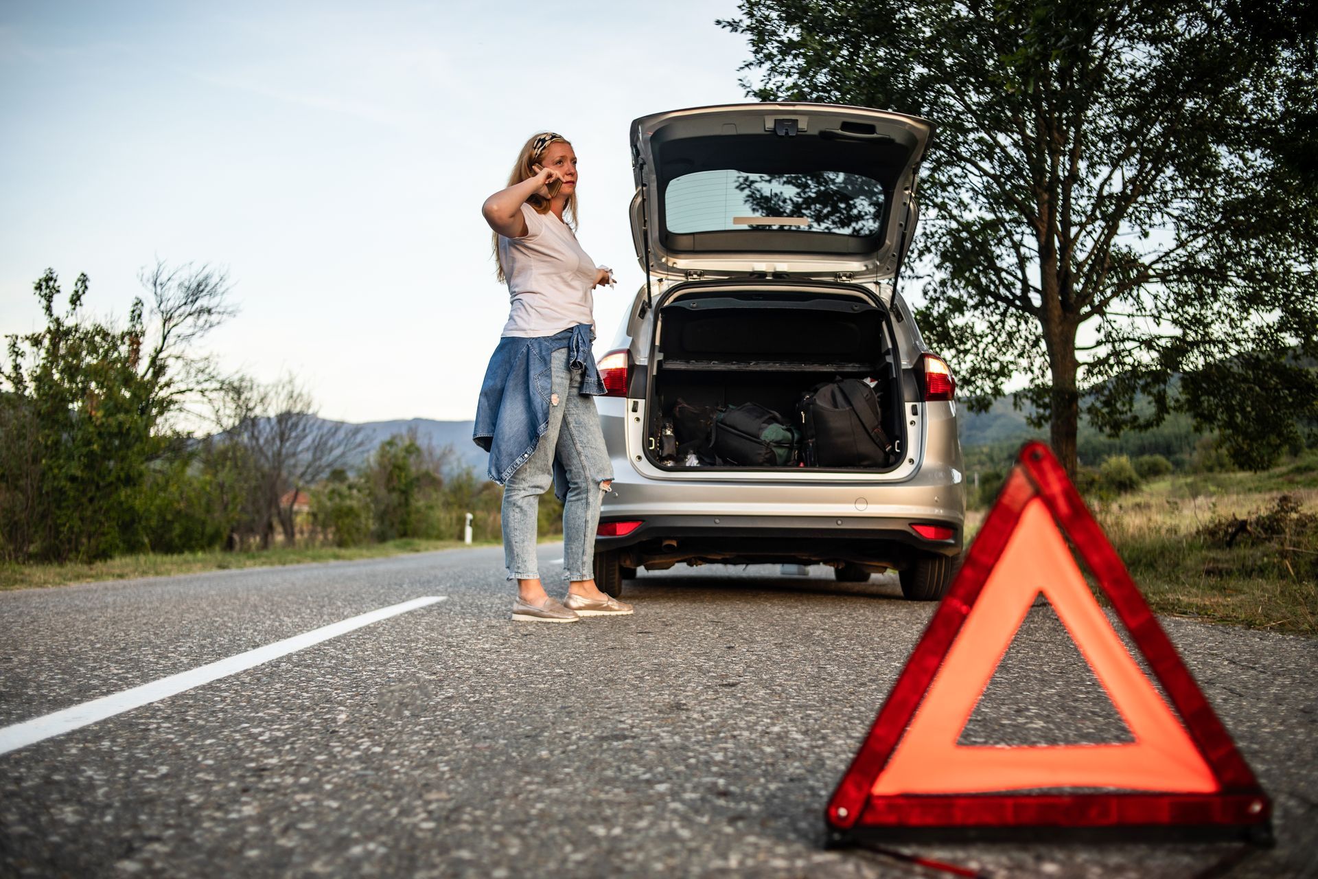 A woman is standing next to a broken down car on the side of the road.