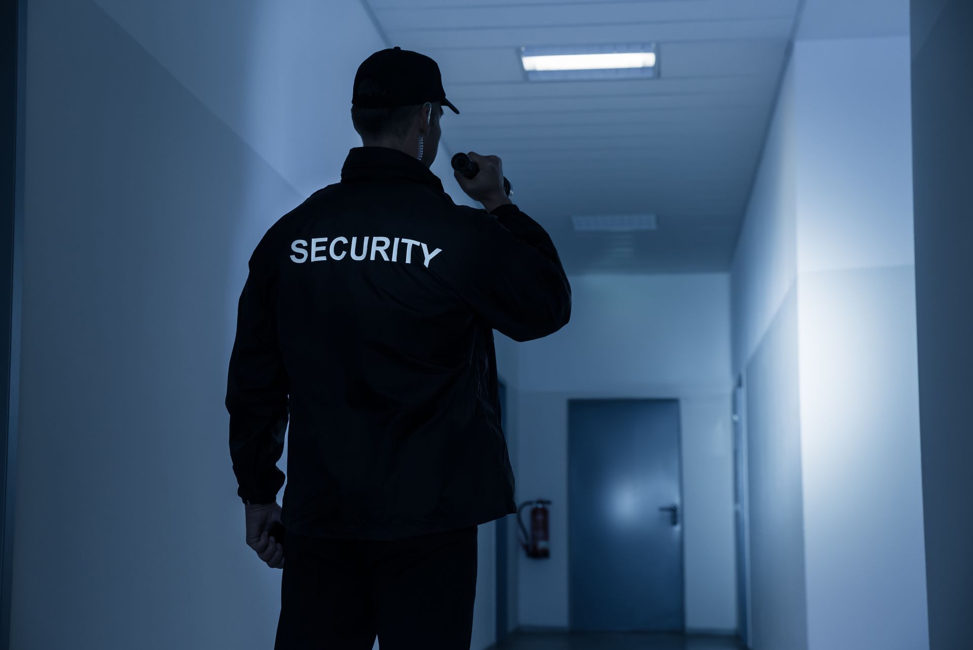 A security guard is standing in a hallway holding a flashlight.