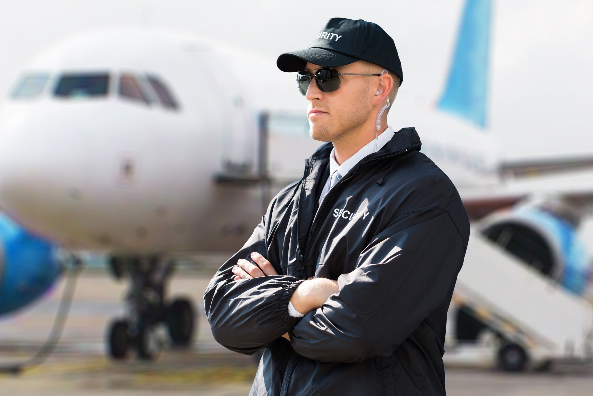 A security guard is standing in front of an airplane with his arms crossed.