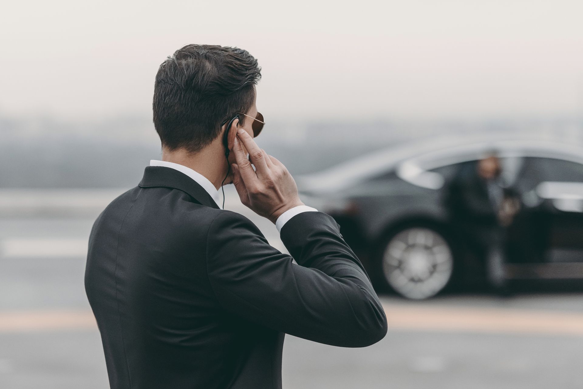 A man in a suit is talking on a cell phone in front of a car.