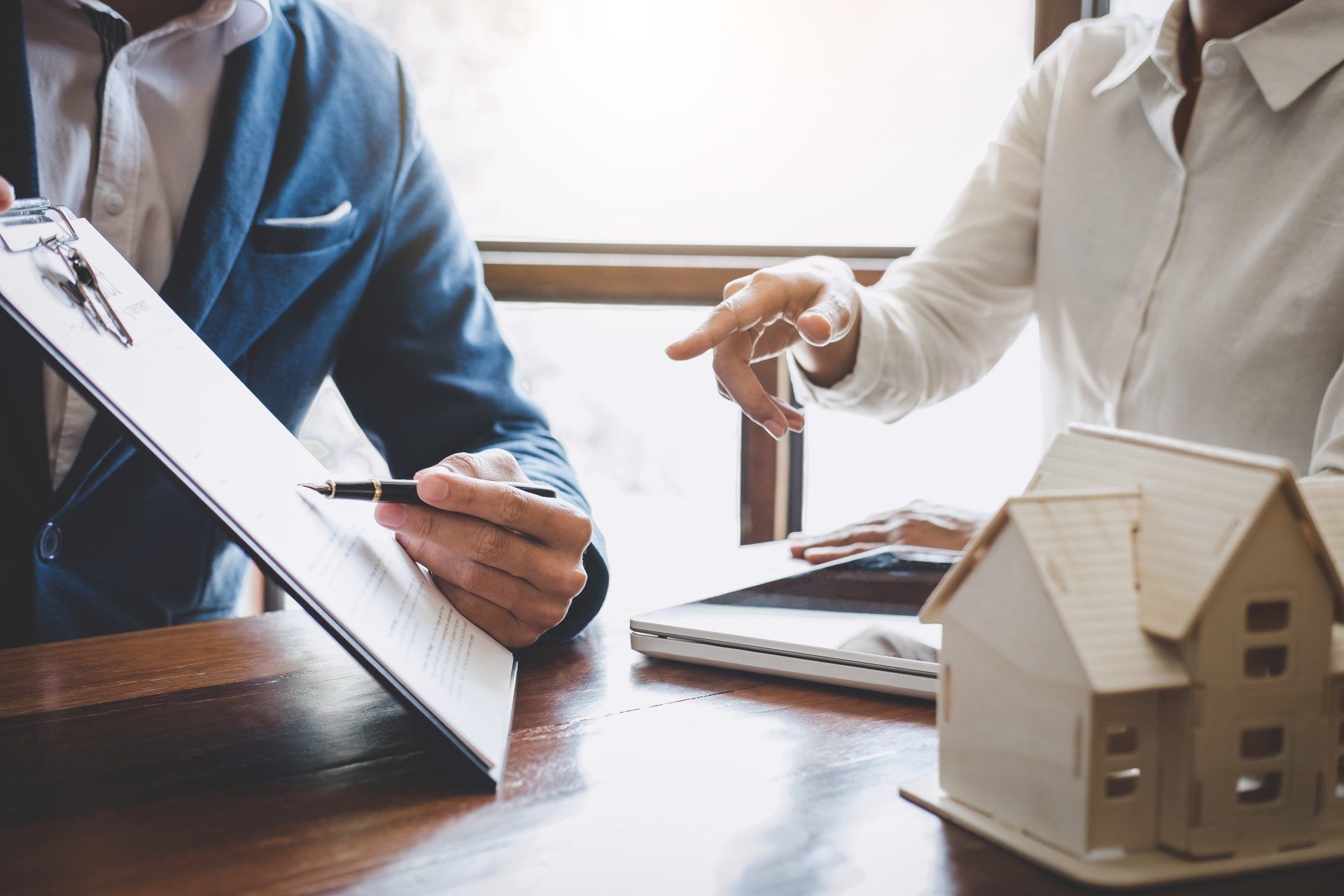A man and a woman are sitting at a table looking at a clipboard and a model house.