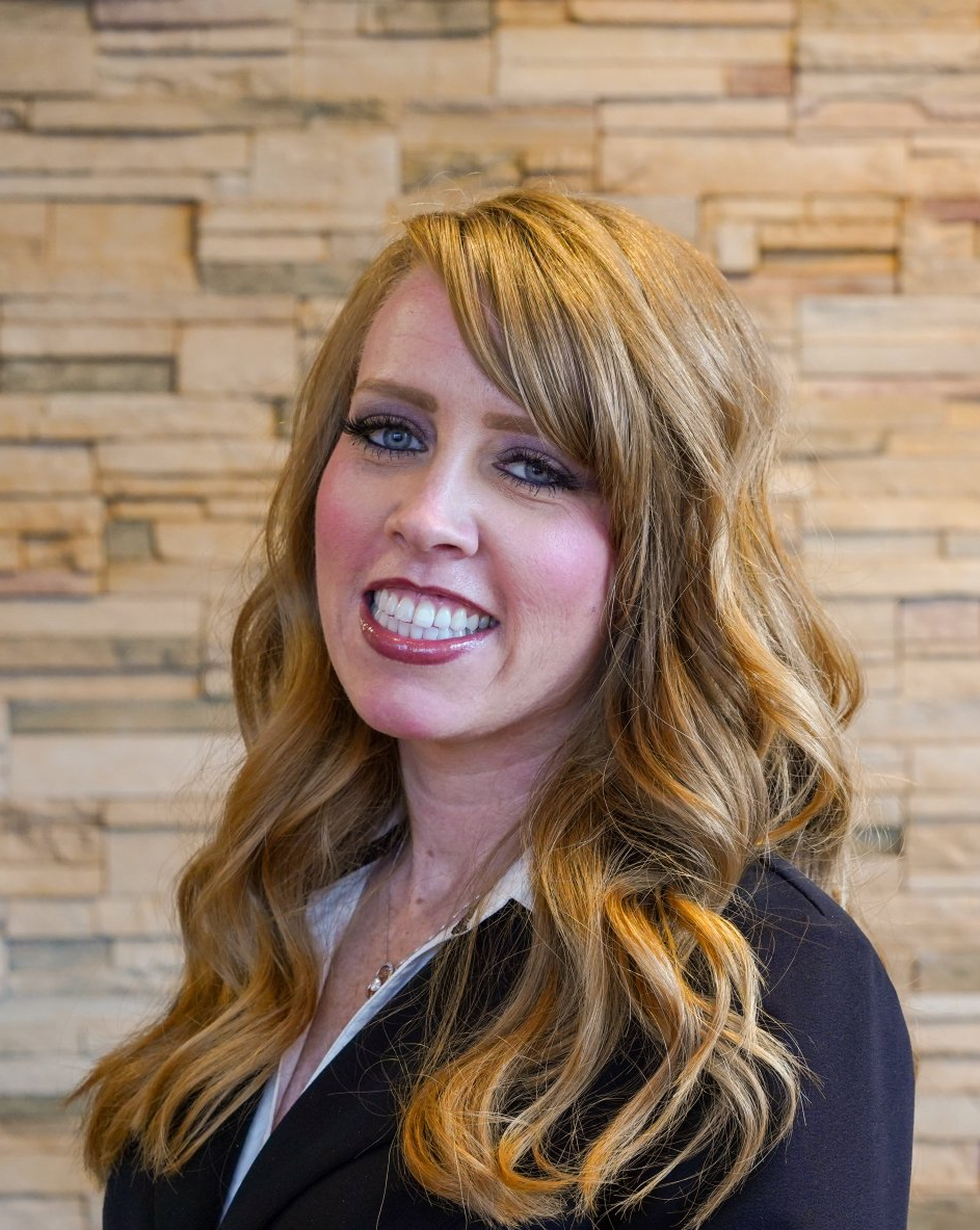 A woman with long hair is smiling in front of a brick wall.