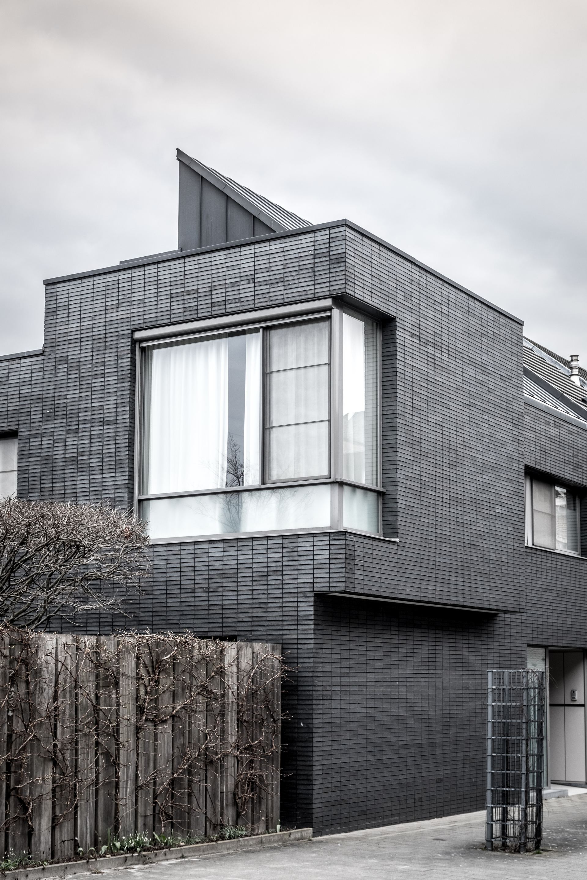 A black and white photo of a modern house with a wooden fence in front of it.