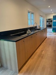 Light wood kitchen cabinets with black countertop. Sink and window visible.