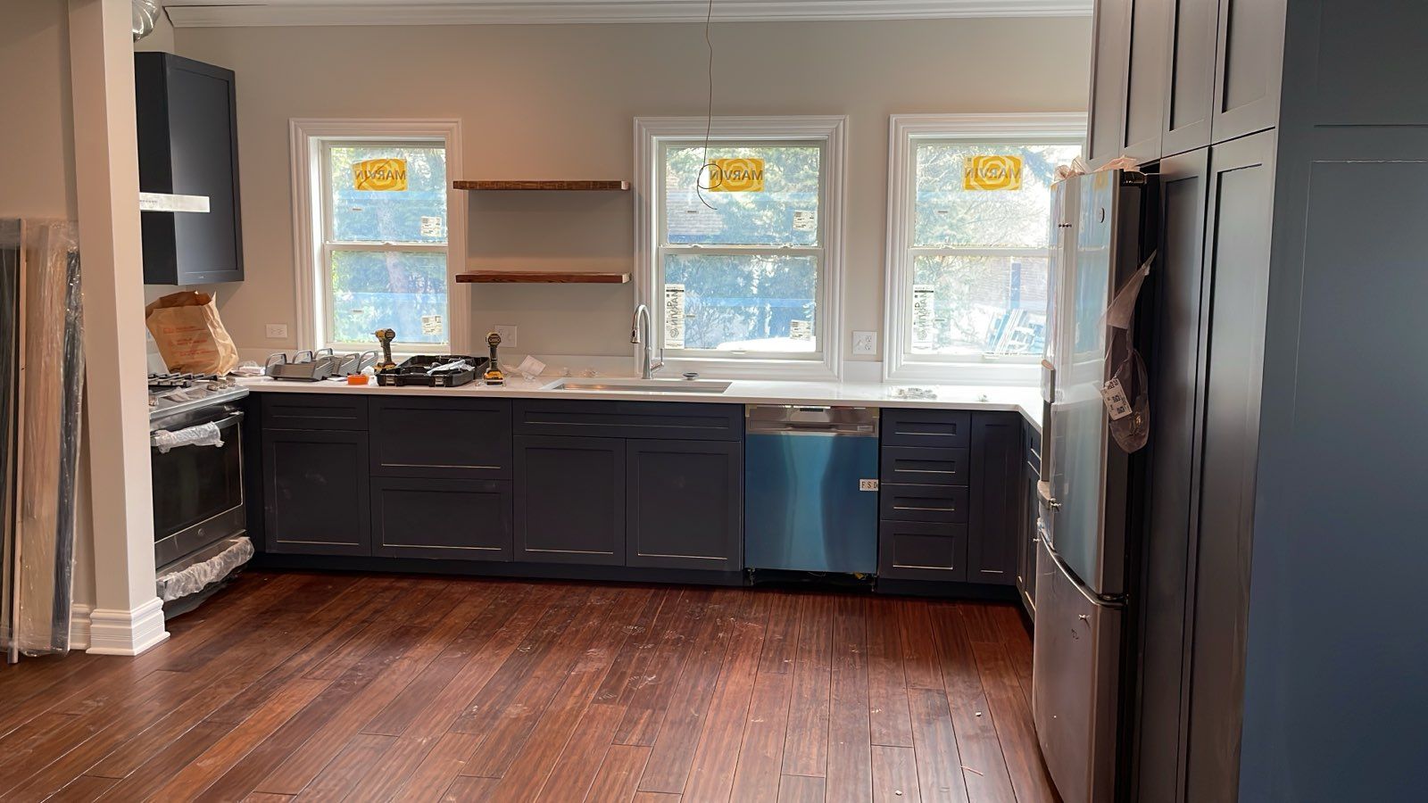 Dark blue kitchen cabinets with windows above a countertop, wood floor, and refrigerator.