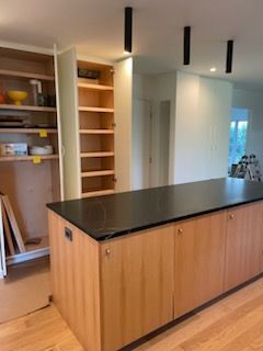 Kitchen with a wood island, black countertop, and light-colored cabinets. Built-in shelving on the left.