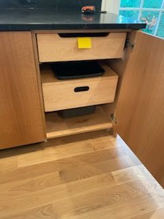 Kitchen cabinet with open door, two wooden drawers, and black countertop.