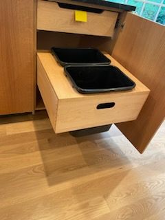 Wooden kitchen cabinet with pull-out trash bins.  One drawer open, revealing two black trash receptacles.