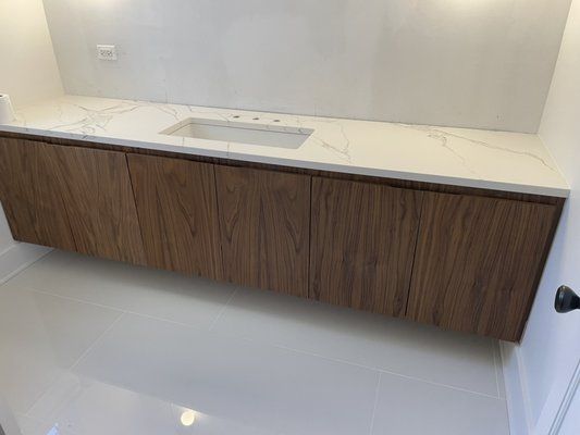 Floating wooden bathroom vanity with marble countertop, white sink, and white walls.