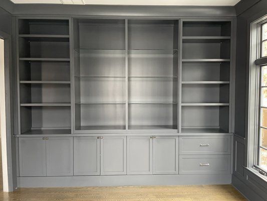 Gray built-in bookcase with shelves and cabinets; next to a window with natural light.