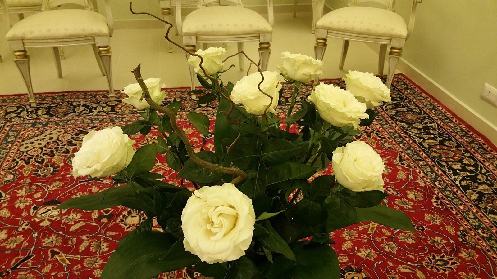 un vaso di rose gialle in una stanza con un tappeto e delle sedie