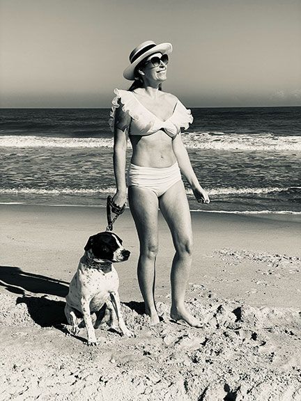 A woman in a bikini is standing next to a dog on the beach.