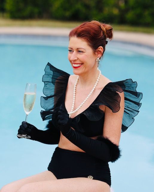 A woman in a black bikini is holding a glass of champagne