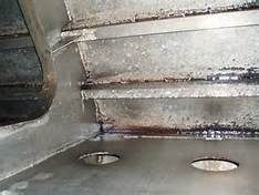 Close-up view of welded metal beams with some discoloration and oval cutouts.