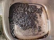 Dark, granular substance submerged in clear liquid within a clear plastic container.