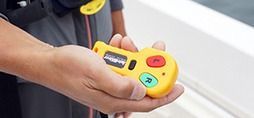 Person holding a yellow remote with red and green buttons, possibly for a boat.
