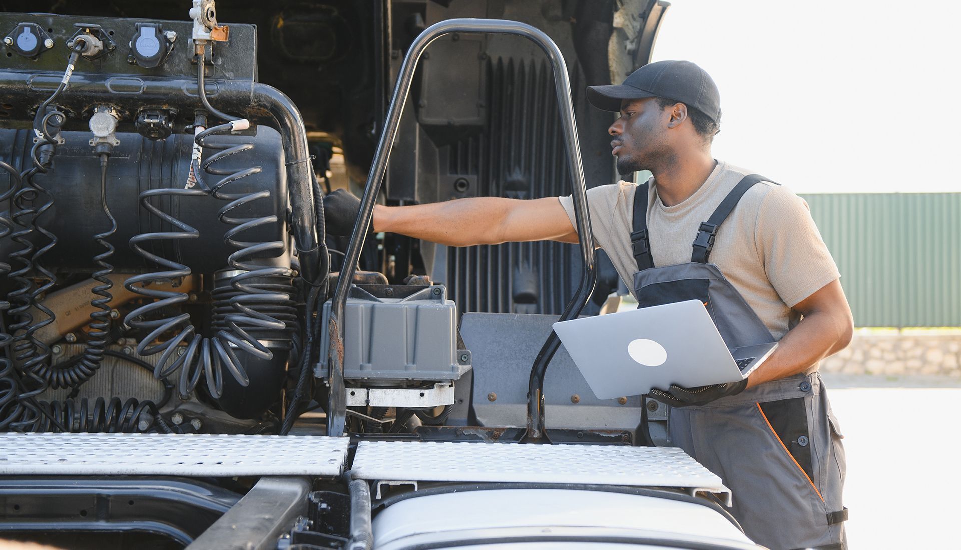 Mechanic inspecting a truck engine with a laptop, outdoors.