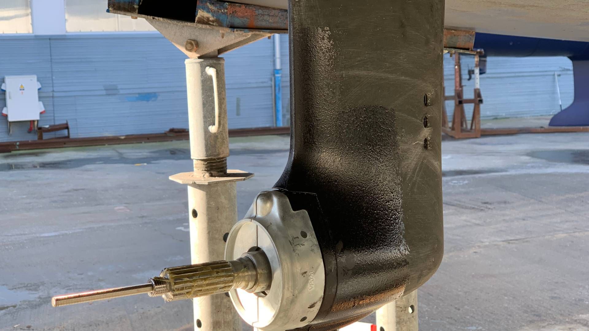 Black painted boat keel with propeller shaft, supported on stands, outdoor setting.