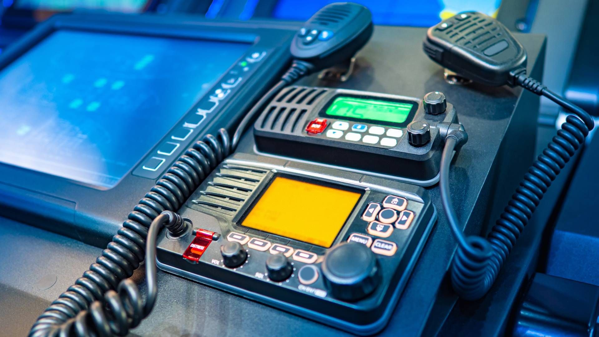 Close-up of a control panel with two-way radios, microphones, and screens, illuminated with blue light.