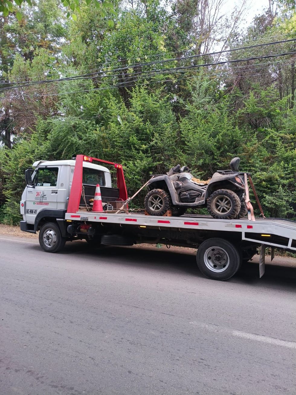 Una grúa blanca estacionada al costado de una carretera transportaba un vehículo todoterreno embarrado en su plataforma.