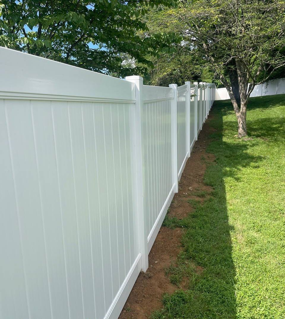 Metal gate and fence on stone wall, leading to a building with trees in the background.