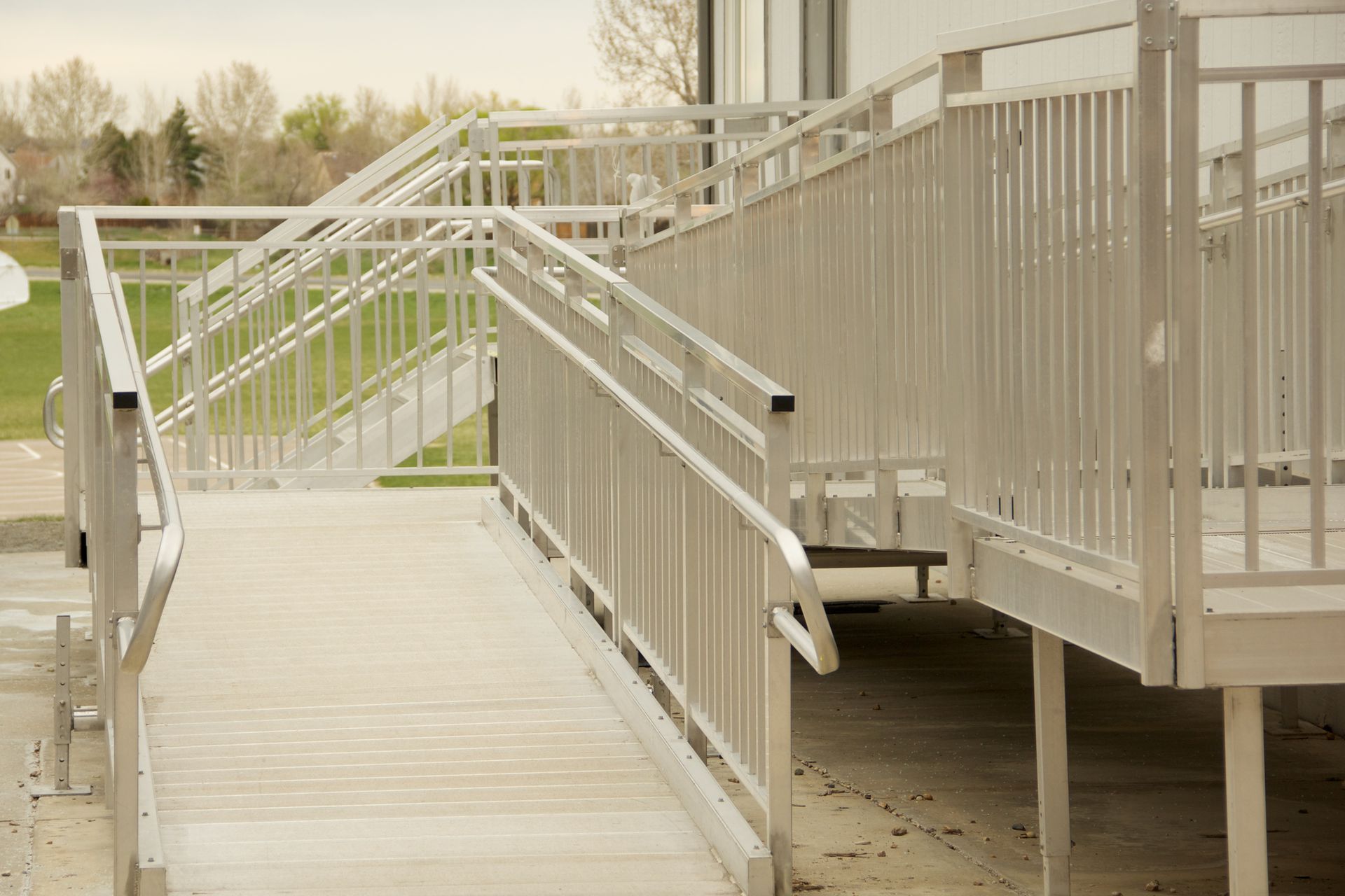 Aluminum ramp and stairs provide access to a building, with railings, on a cloudy day.