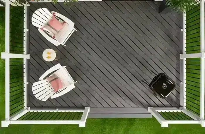 Overhead view of a gray deck with white chairs, a small table, and a grill, surrounded by green grass and white railings.