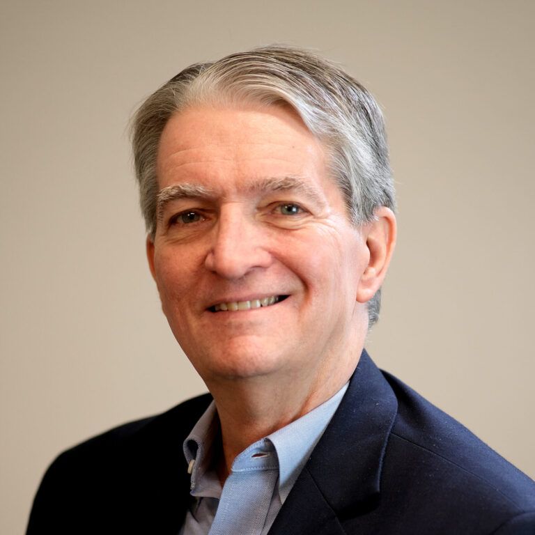 A man in a suit and blue shirt is smiling for the camera.