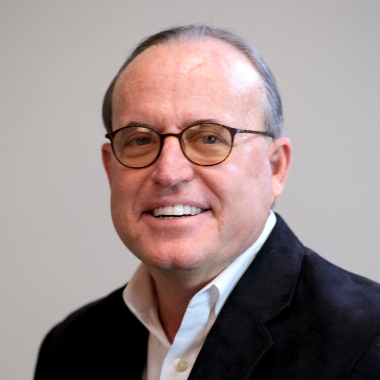 A man wearing glasses and a suit smiles for the camera