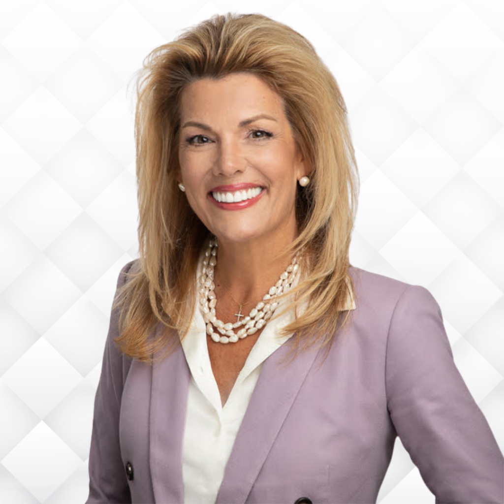 A woman in a purple suit and pearl necklace is smiling.
