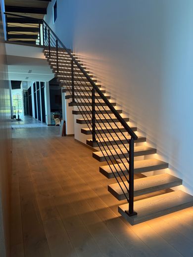 A modern staircase with light-colored floating treads, illuminated by integrated LED strips, featuring a black railing.