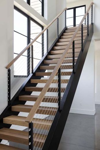 A modern staircase with light wood treads, black metal stringers, and a cable railing system against white walls.