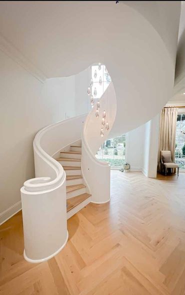 A bright interior features a white, curved staircase with light wood steps and a modern, cascading glass chandelier.