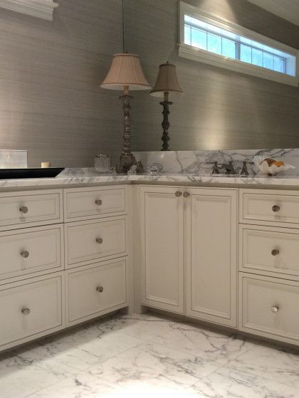 A modern bathroom vanity with cream-colored cabinets, marble countertops, and a tall lamp against a gray textured wall.