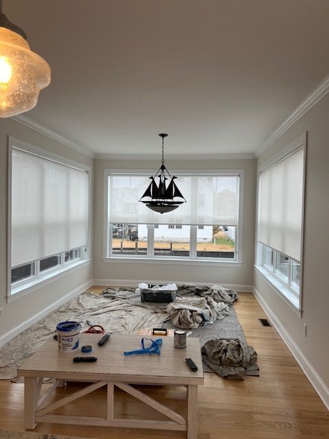 Dining room with roller shades, white trim, and a center light fixture.  A table is set up with painting supplies.