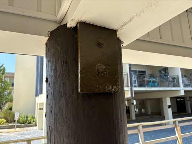 Dark brown wooden pillar with a painted metal bracket securing a white beam to a deck.