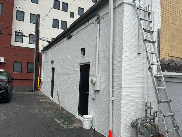 White brick building with two black doors, ladder, and parked car.