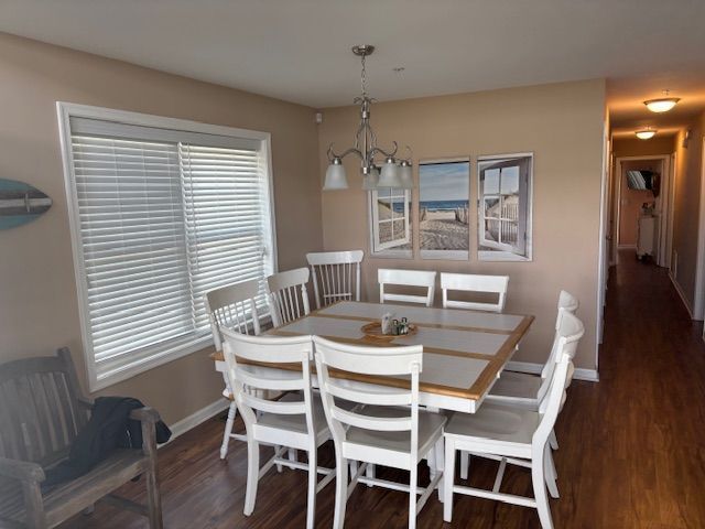 Dining room with a white table and chairs, a beach scene artwork, and a window with blinds.