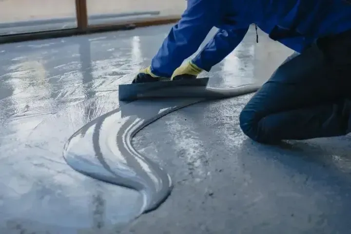 Person smoothing grey epoxy flooring with a trowel, kneeling indoors.