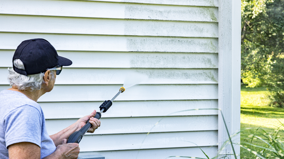 Person power washing a white house siding with a spray nozzle.