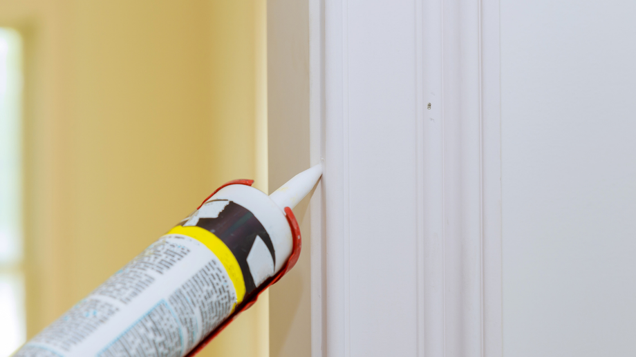 Caulk gun applying sealant to white door frame.