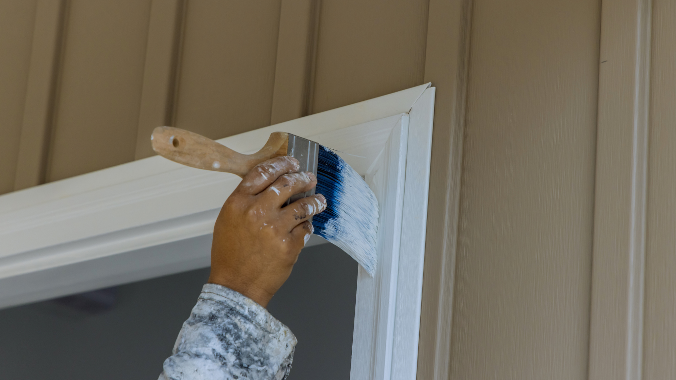 Hand holding blue paint roller against a blue wall, applying paint.
