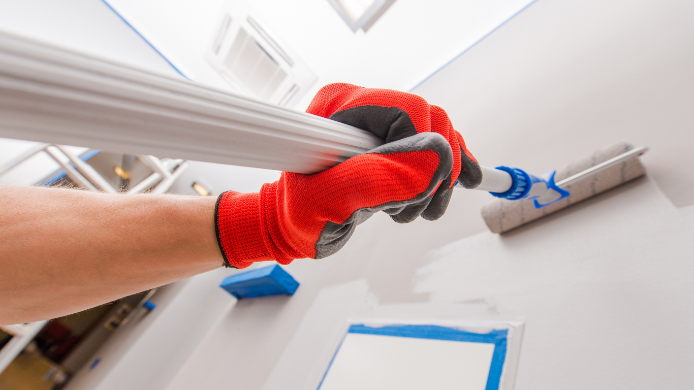 Person painting a white wall blue with a paint roller.