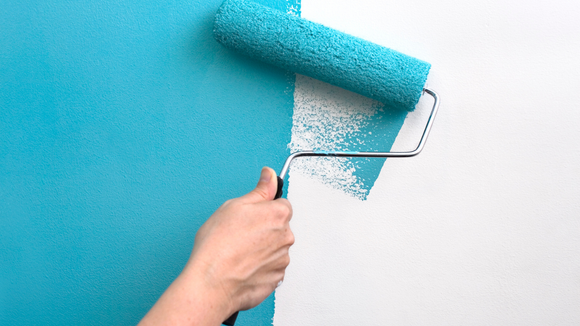 Hand painting a white wall with a blue paint roller.